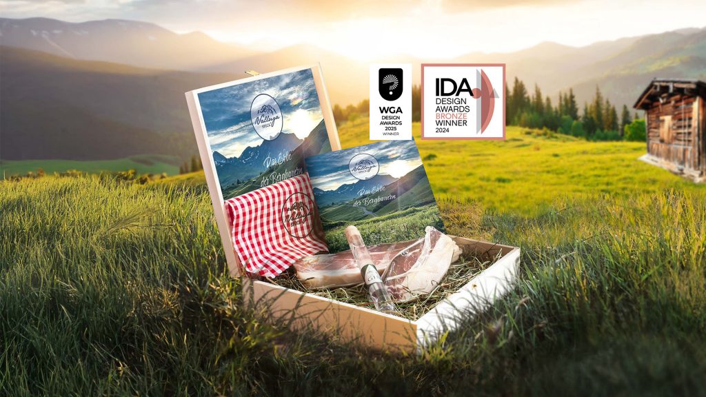 Holzbox auf einer Bergwiese mit hochwertigem Speck, Gin und einer Broschüre. Zwei Auszeichnungen von Design Awards. IDA Design Awards Bronze Winner 2024, WGA Design Awards 2025 Winner